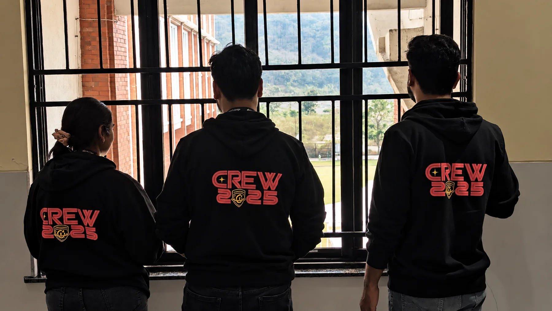 Three crew members from behind in black hoodies printed CREW 2025 with the shield logo