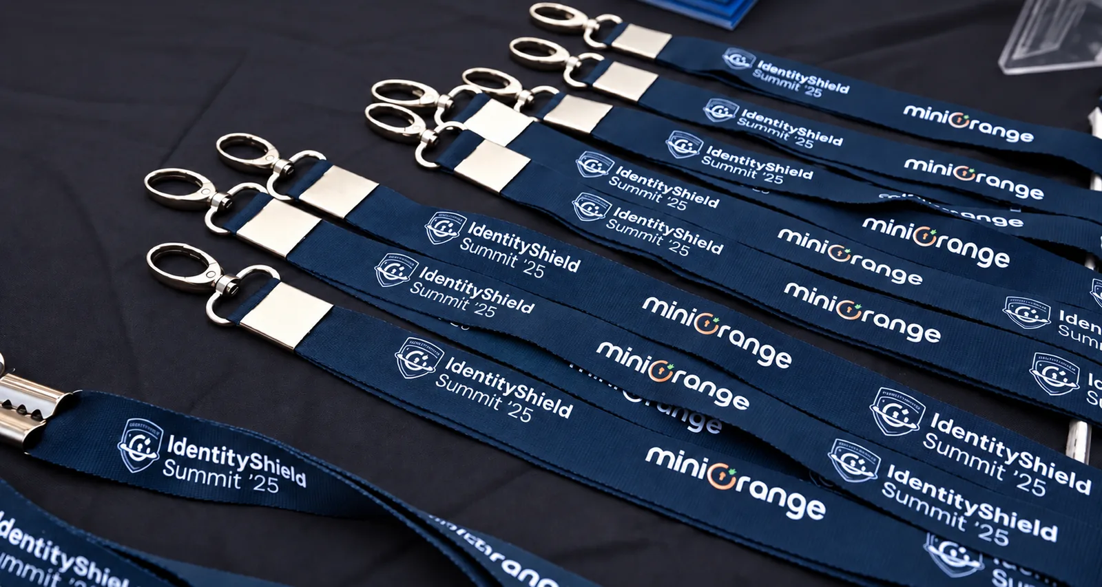 Navy IdentityShield Summit ’25 lanyards with silver clips laid out on a black table
