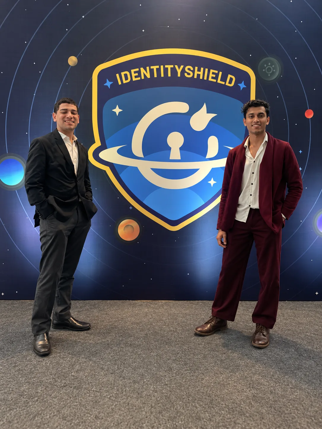 Two men in suits standing either side of the Identity Shield logo backdrop