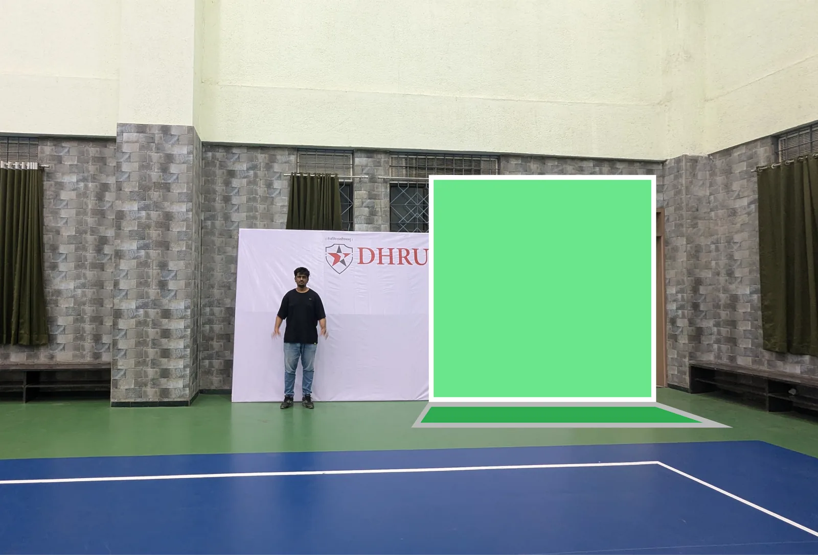 A person standing next to an existing backdrop in the hall, with a green block marking where a planned booth wall would stand