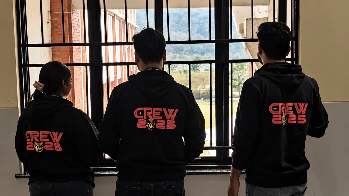 Three people from behind in black hoodies printed with CREW 2025